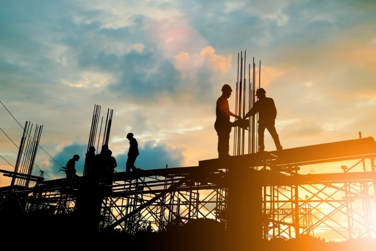 Construction workers on scaffolding silhouetted at sunset